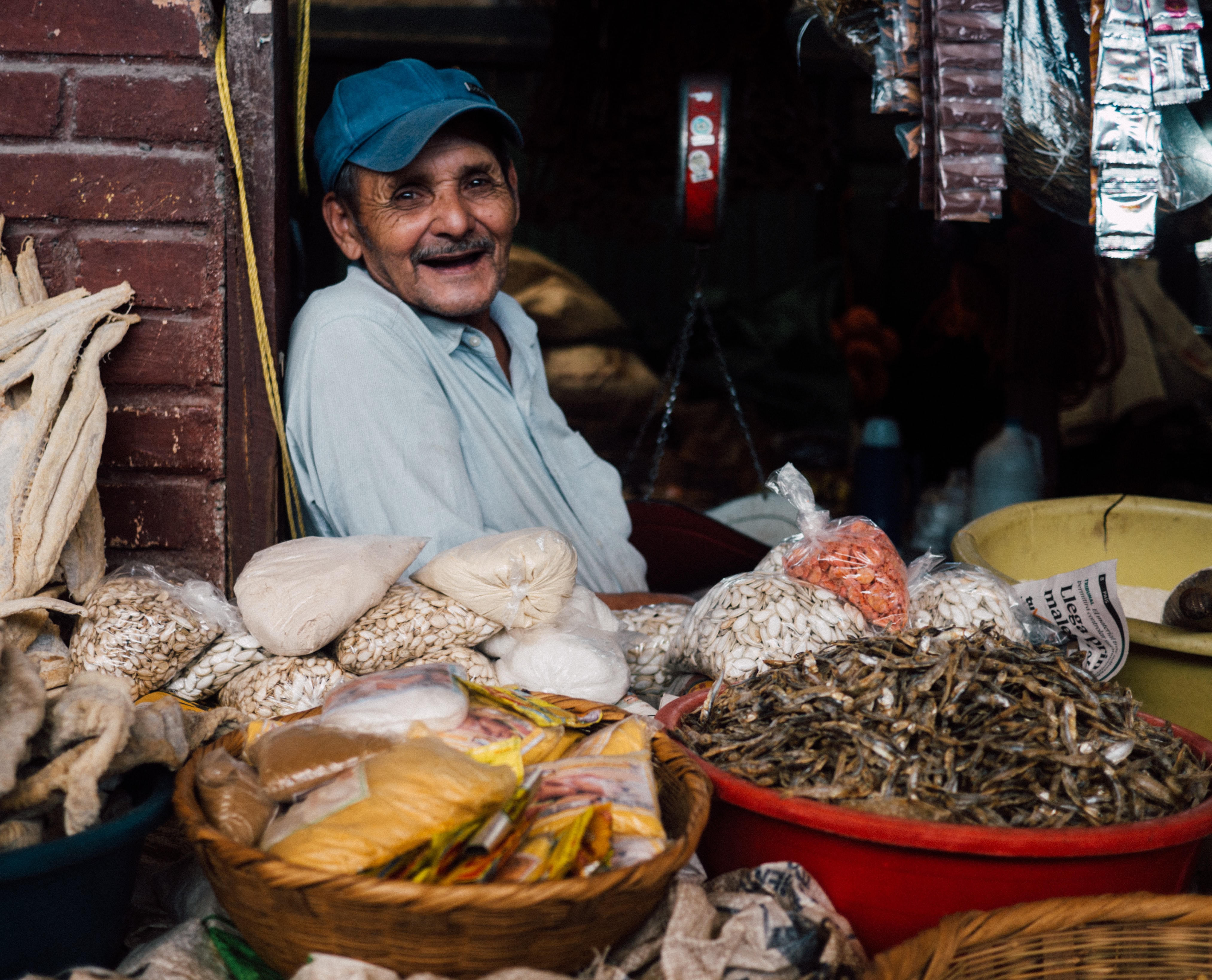 photo of man in his 50's or 60's surrounded by bowls of grains and food supplies in a Honduran market