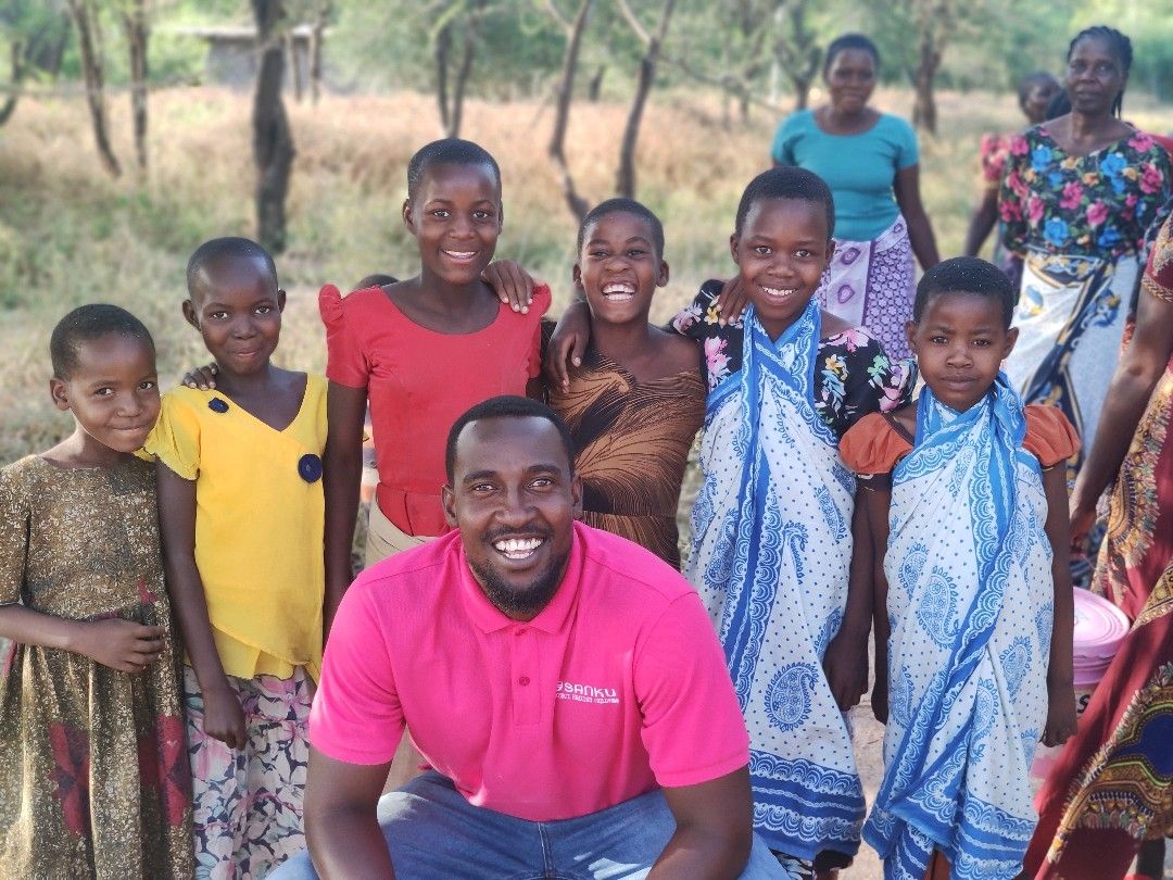 photo of Sanku representative with group of children dressed in bright colors smiling