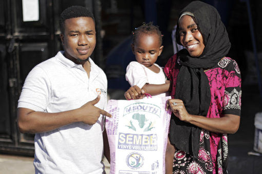 Sanku rep stands with a young mother and toddler while pointing at a bag of flour