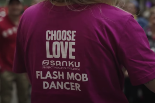 Woman with magenta t-shirt that says Choose Love Sanku Project Healthy Children Flash Mob Dancer on the back in white lettering